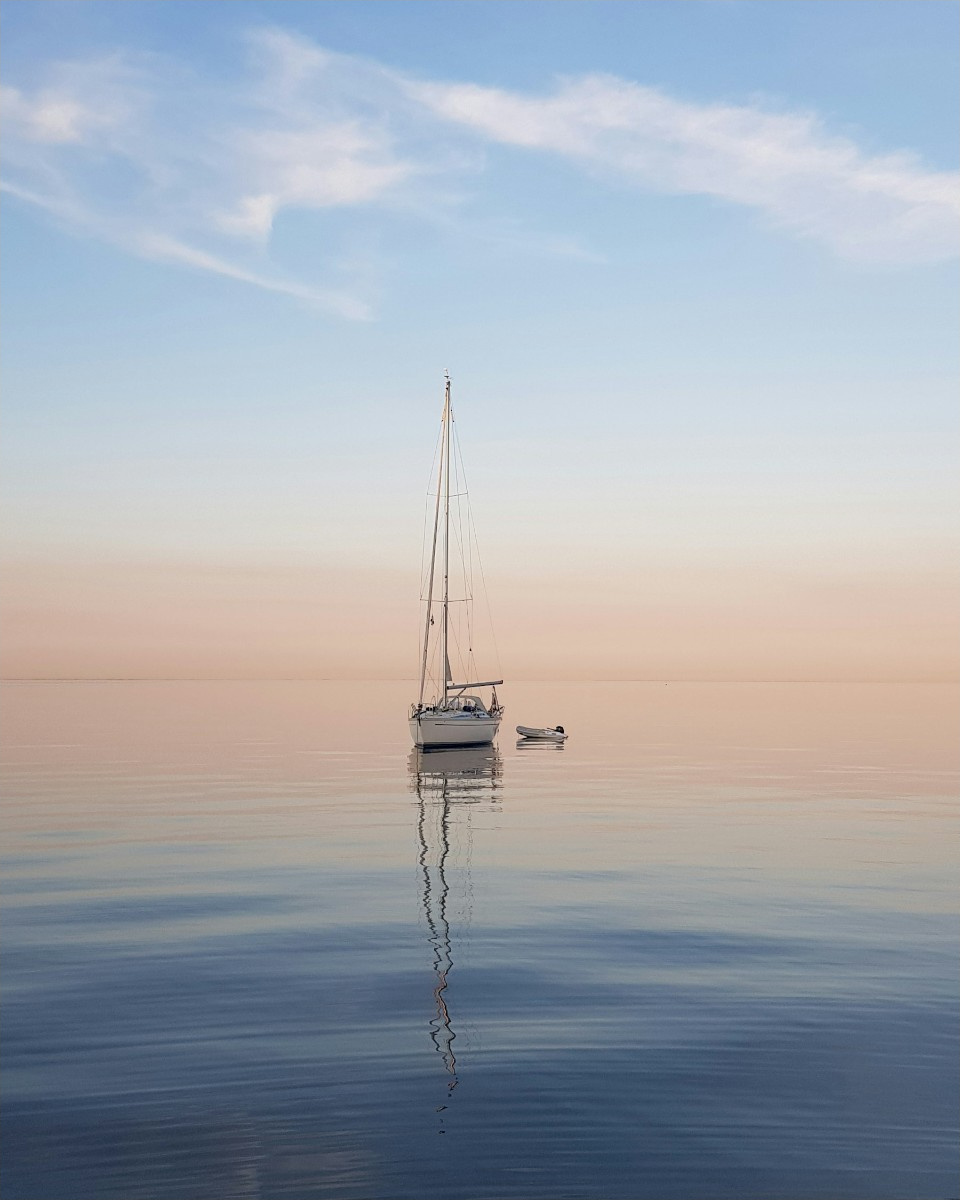 A sailboat anchored on calm water at dusk